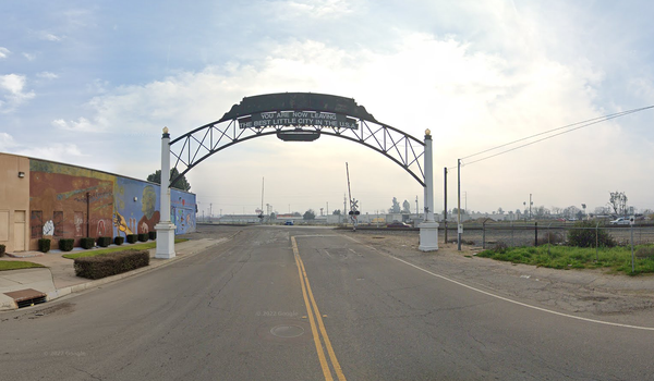 Arch with sign reading "you are now leaving the best little city in the USA" in front of a mural & industrial train tracks